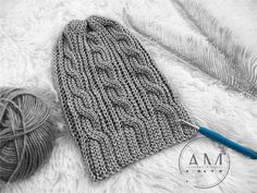 a gray knitted mitt next to a ball of yarn and a blue crochet hook