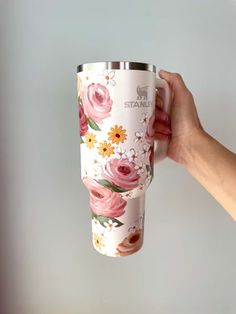 a hand holding a coffee cup with pink flowers on the outside and white inside, in front of a gray wall