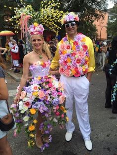 two people dressed up in costumes and holding flowers on the street with confetti