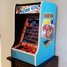 an old arcade machine sitting on top of a wooden table next to a white wall