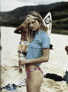 a woman in a blue shirt and pink panties holding a water bottle on the beach