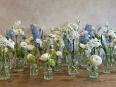 there are many glass vases with flowers in them on the wooden table and one is empty