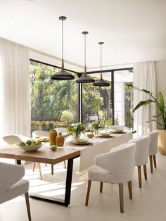 a dining room table with white chairs and green fruit on the plates in front of it