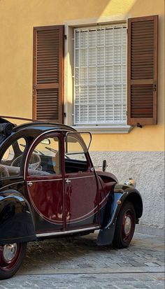 an old fashioned car parked in front of a building with shutters on the windows