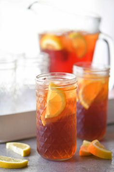 two mason jars filled with iced tea and sliced lemons on a counter top next to a pitcher