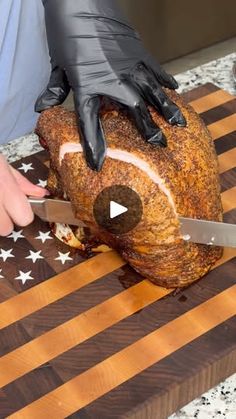 a person in black gloves cutting up a large piece of meat on top of a wooden board