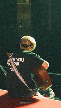 a man sitting on top of a table with a guitar in his lap and looking at the ground