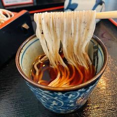 chopsticks sticking out of a bowl filled with noodles and sauce on a table