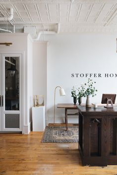 an office with white walls and wooden flooring is pictured in this image, there are two vases on the desk