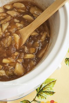 a white crock pot filled with stew and a wooden spoon sitting in the bowl