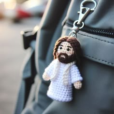 a crocheted jesus keychain hanging from the side of a backpack,