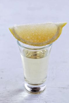 a lemon wedge is sticking out of a shot glass filled with water and sugar on a white surface