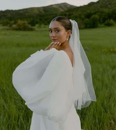 a woman in a white wedding dress standing in a field with her hands on her face