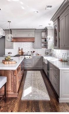 a large kitchen with gray cabinets and white counter tops, wooden flooring and an area rug on the hardwood floor