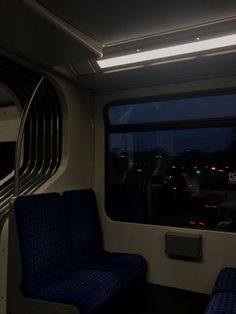 two blue seats in front of a window on a train at night with the lights on