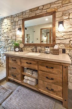 a bathroom with stone walls and wooden cabinets, including a large mirror over the sink