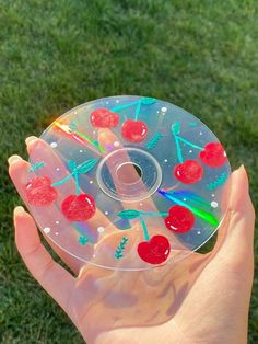 a hand holding a clear plastic disc with cherries on it in the grass,