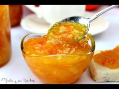 a spoon full of jelly sitting next to some bread on a white plate and sauce in a glass bowl