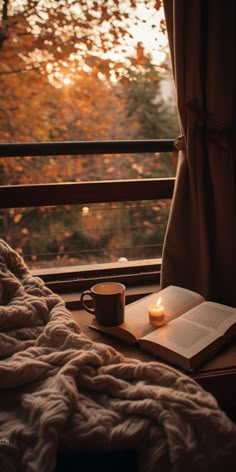 an open book and cup on a window sill with the sun setting in the background