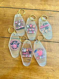 six keychains with different designs on them sitting on a wooden table, one has the words hello kitty written on it