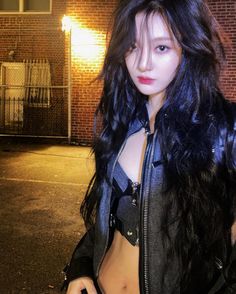 a woman with long black hair and leather jacket standing in front of a brick building