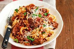 a white plate topped with pasta and meat covered in marinara sauce, parmesan cheese