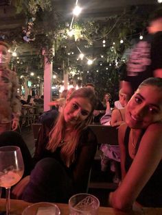 two women sitting next to each other at a table with wine glasses in front of them