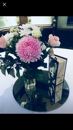 a vase filled with pink and white flowers sitting on top of a table next to an open book