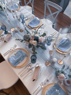 the table is set with blue and gold plates, silverware, flowers and candles