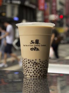 a cup of coffee sitting on top of a table in front of people walking down the street