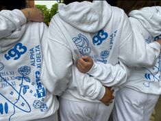 three people in white hoodies with blue letters on them and one person holding his hands behind his back