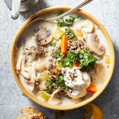 a bowl of soup with mushrooms, carrots and other vegetables next to a piece of bread