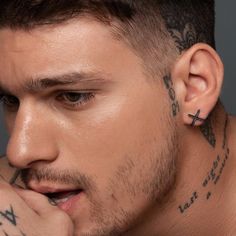 a man with tattoos and piercings on his ear looking at the camera while holding his hand to his chin