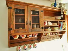 an old wooden hutch filled with dishes and cups on top of a wall mounted shelf