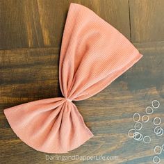 a pink bow tie sitting on top of a wooden table next to some silver rings