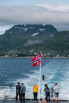 people standing on the deck of a boat looking out at water and mountains in the distance