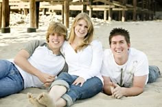 three people are sitting on the sand together and smiling at the camera while posing for a photo