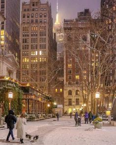 people are walking in the snow near tall buildings and street lamps at night with lights on