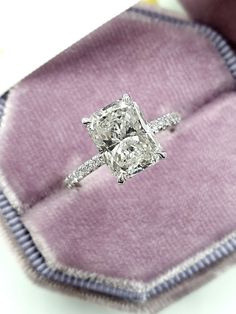 a cushion cut diamond ring sits on top of a purple velvet case