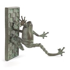 a statue of a frog climbing up the side of a wall with its legs spread out