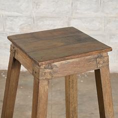 an old wooden stool sitting in front of a white brick wall with no one on it