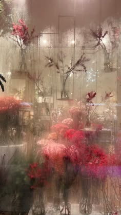 flowers in vases are seen through a window with rain falling on them and behind them is an image of trees