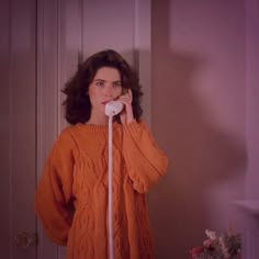 a woman in an orange sweater is talking on the phone while holding a white cord