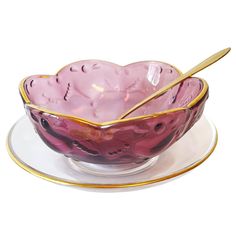 a pink bowl and saucer with gold trimmings on a white plate next to a spoon