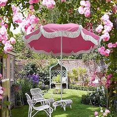 an open umbrella in the middle of a garden with lawn chairs and pink flowers around it