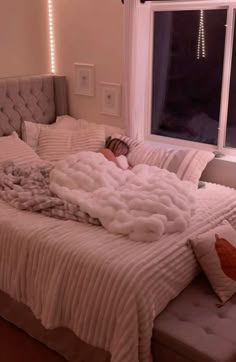 a person is sleeping on a bed with white sheets and pillows in front of a window