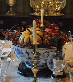 a bowl with candles and pumpkins in it sitting on a table next to wine glasses