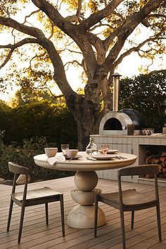 an outdoor table with two chairs and a pizza oven in the background