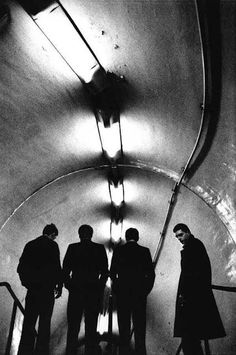 three men are standing on the escalator and looking at something in the distance