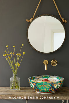 a bathroom sink sitting under a round mirror next to a vase with flowers in it